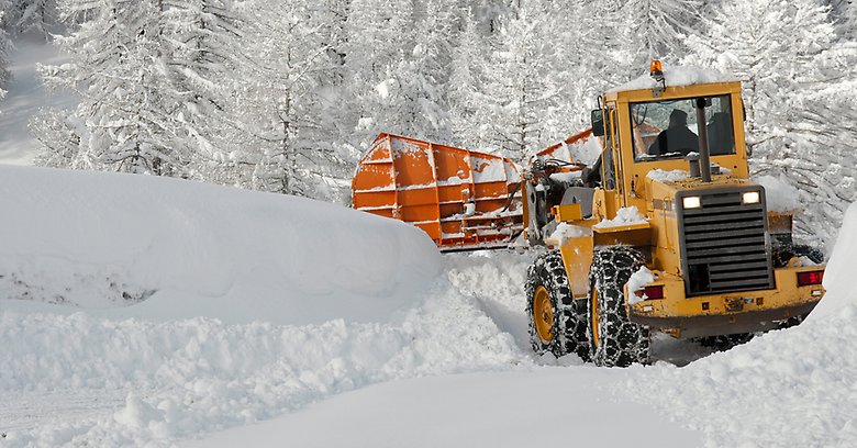 Gul traktor röjer stora mängder snö.